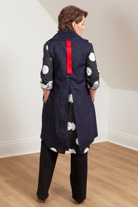 Woman wearing a navy blue vest (Melva - back view) over a patterned shirt in a room with white walls and wooden floor. 