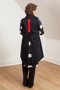 Woman wearing a black vest (Melva - back view) over a patterned shirt in a room with white walls and wooden floor. 