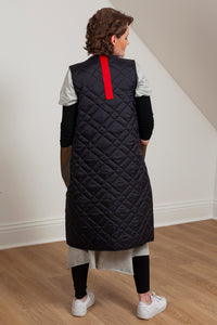 Woman wearing a quilted vest with oversized faux leather pockets. Back view