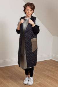 Woman wearing a quilted vest with oversized faux leather pockets. Front view with hands on vest sides.