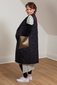 Woman wearing a quilted vest with oversized faux leather pockets. side view