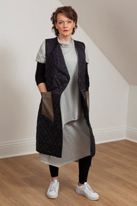 Woman wearing a quilted vest with oversized faux leather pockets. Front view